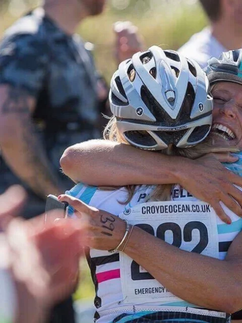 Two cyclists in helmets, one wearing Propello branding, hugging each other