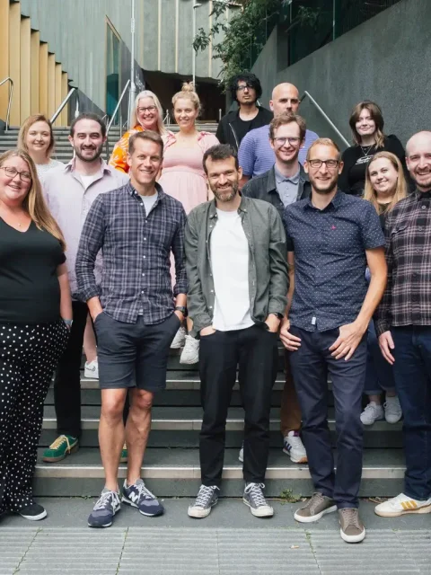 Craft CMS agency Webdna team members are standing up together with smiles.