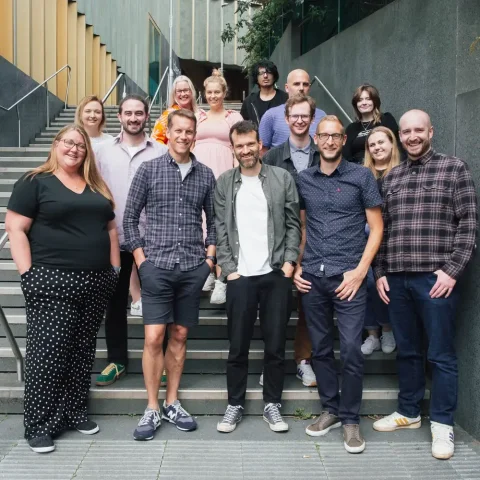 Craft CMS agency Webdna team members are standing up together with smiles.